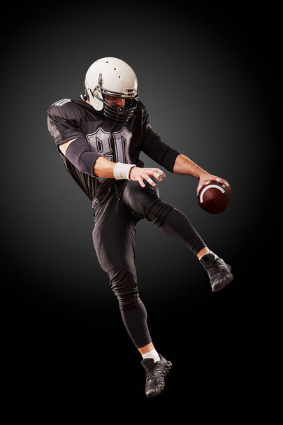 Американский футболист в прыжке с мячом на черном фоне
 - Фото, изображение