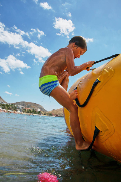 Menino brincando no trampolim de água no mar no dia ensolarado
 - Foto, Imagem