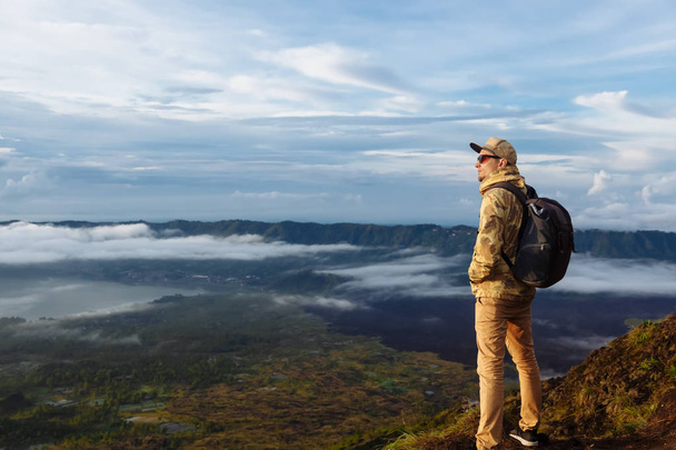 L'uomo turista guarda l'alba sul vulcano Batur sull'isola di Blai in Indonesia. Escursionista uomo con zaino viaggio sul vulcano superiore, concetto di viaggio
 - Foto, immagini