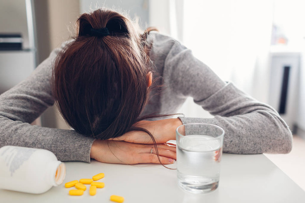Młoda kobieta zdenerwowany i zmęczony biorąc pigułki przeciw chorobie w kuchni. Kobieta płacze. Opieka zdrowotna i medycyna - Zdjęcie, obraz