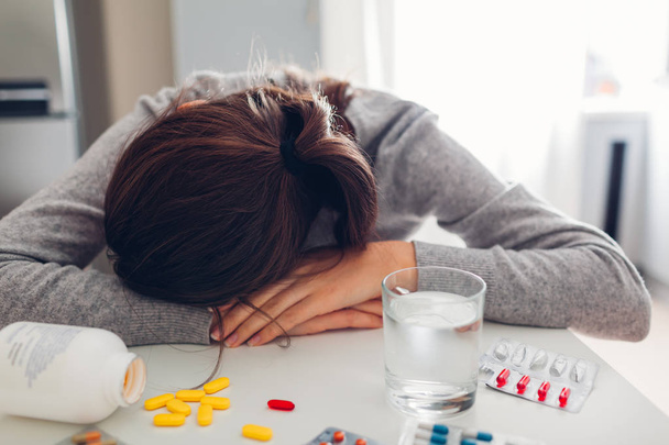 junge Frau aufgebracht und müde von Tabletten gegen die Krankheit in der Küche. Frau weint. Gesundheitswesen und Medizin - Foto, Bild