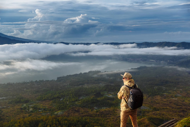 Homem turista olha para o nascer do sol no vulcão Batur na ilha de Blai, na Indonésia. Caminhante homem com mochila viajar no topo vulcão, conceito de viagem
 - Foto, Imagem
