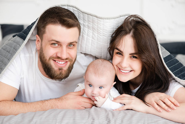 Νέα χαμογελαστή οικογένεια με κόρη υπό κουβέρτα - Φωτογραφία, εικόνα
