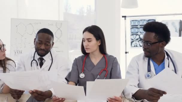 Team of multiethnic young doctors having a meeting in conference room in the modern hospital. Group of multiethnic doctors are medical studying studying disease histories patients - Materiaali, video