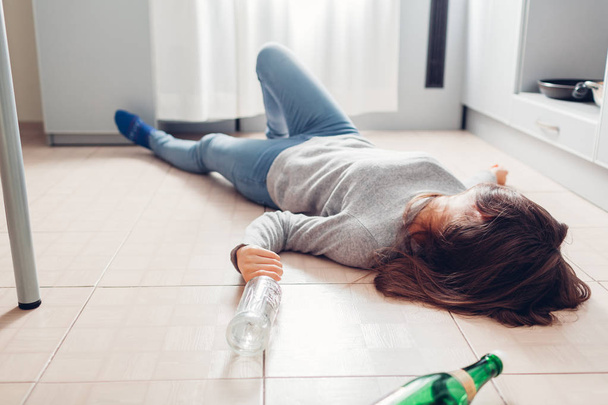 Kobieta uzależnienie od alkoholu. Młoda kobieta śpi na podłodze w kuchni po imprezie otoczonej butelkami wina - Zdjęcie, obraz
