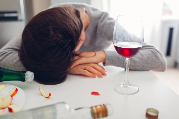 Kobieta uzależnienie od alkoholu. Młoda kobieta śpi na stole kuchennym otoczonym butelkami wina - Zdjęcie, obraz