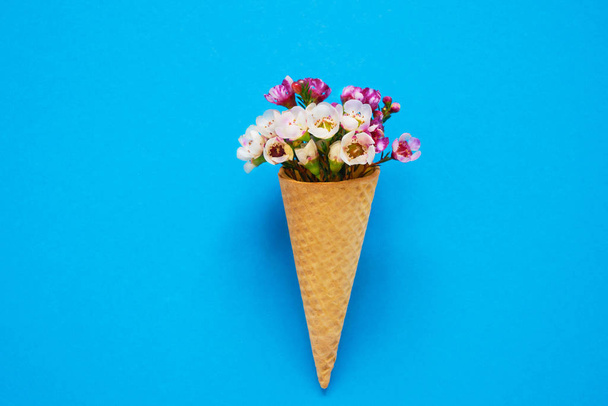 青い背景に小さな花を持つアイスクリームコーン。コピー領域、上面図. - 写真・画像