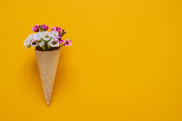 Ice cream cone with small flowers on yellow background. Copy space, top view. - Foto, afbeelding