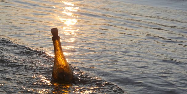 Butelka z wiadomością na wodzie o zachodzie słońca - Zdjęcie, obraz