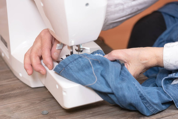 Gros plan des mains de femme âgée couturière jeans à coudre sur machine à coudre électrique
. - Photo, image