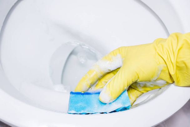 τα χέρια στα κίτρινα γάντια καθαρίζοντας ένα WC. Καθαρισμός του μπλε σφουγγαραριού - Φωτογραφία, εικόνα