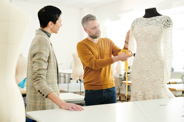 グループで現代のファッションデザイナーは、新しいコレクションからダミーに彼のクライアントの白いレースのドレスを示す - 写真・画像