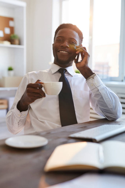 junger erfolgreicher Makler oder Banker in Formalbekleidung, der am Arbeitsplatz Tee oder Kaffee trinkt und in der Pause telefoniert - Foto, Bild