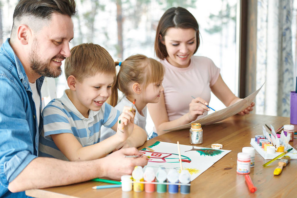 Jovem pai e seu filho quadro de pintura em papel com guache de várias cores, enquanto menina e mãe desenho com lápis de cor por perto
 - Foto, Imagem
