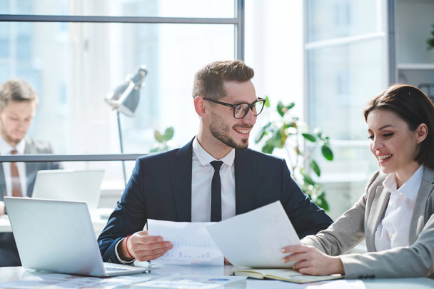 Twee jonge elegante economen in formalwear zittend op werkplek tijdens het bespreken van financiële papers tijdens meeting - Foto, afbeelding