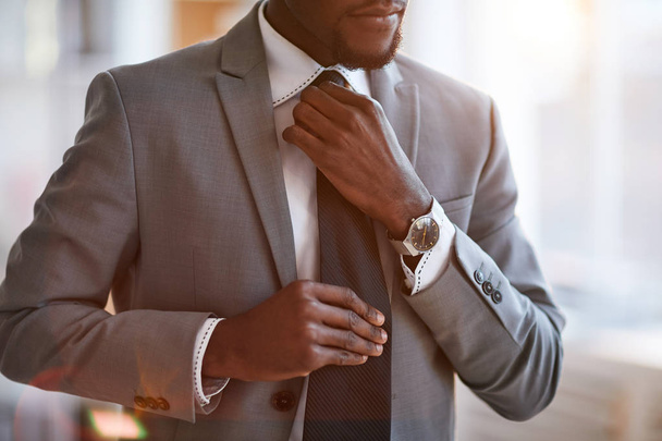 Jovem elegante empresário afro-americano em terno cinza amarrando gravata preta sobre camisa branca
 - Foto, Imagem