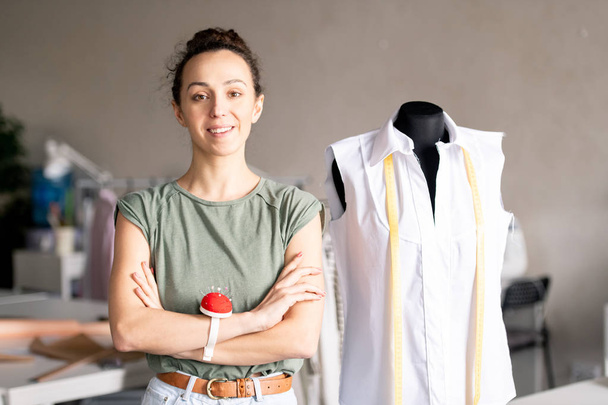 Młoda brunetka kobieta z rękami skrzyżowane na klatce piersiowej stojący przez manekina przed kamerą w Studio mody - Zdjęcie, obraz