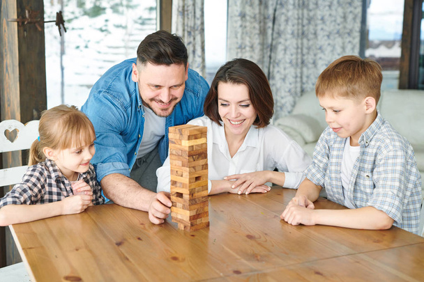 Mladý muž, který si vezme jednu z dřevěných cihel věže, zatímco bude hrát na stole s rodinou - Fotografie, Obrázek