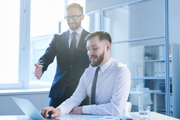 Два молодых успешных бизнесмена в формальной одежде обсуждают онлайн-данные на дисплее ноутбука на рабочей встрече
 - Фото, изображение