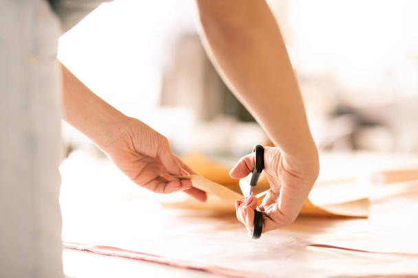 Cucitrice con forbici che si piega sul tavolo e taglia il modello di carta mentre lavora in sartoria
 - Foto, immagini