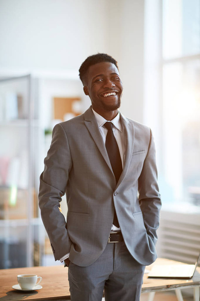 Młody śmiech Afroamerykanin biznesmen w formalwear stoi przed kamerą w biurze - Zdjęcie, obraz