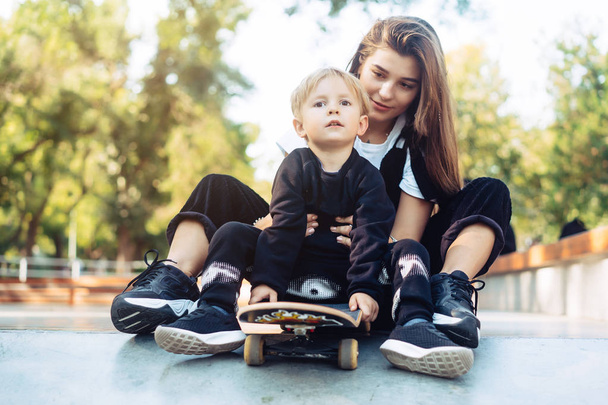 Junge Mutter bringt ihrem kleinen Jungen das Skateboardfahren bei - Foto, Bild