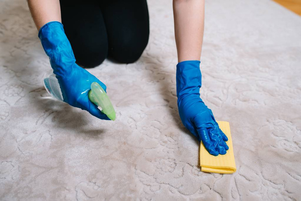 people, housework and housekeeping concept - close up of woman in rubber gloves with cloth and derergent spray cleaning carpet at home. close up of woman with cloth cleaning carpet - Zdjęcie, obraz