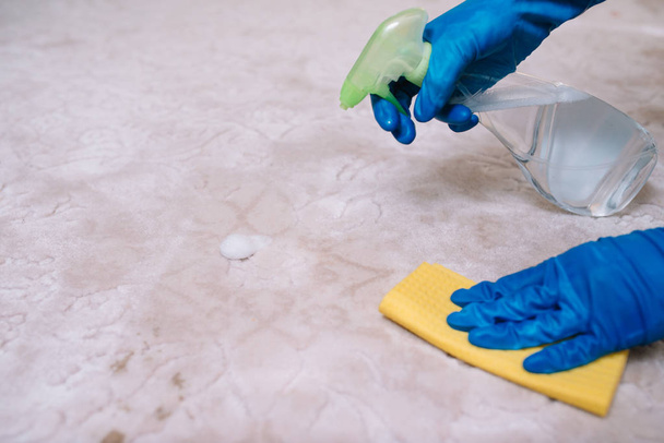 people, housework and housekeeping concept - close up of woman in rubber gloves with cloth and derergent spray cleaning carpet at home. close up of woman with cloth cleaning carpet - Foto, imagen