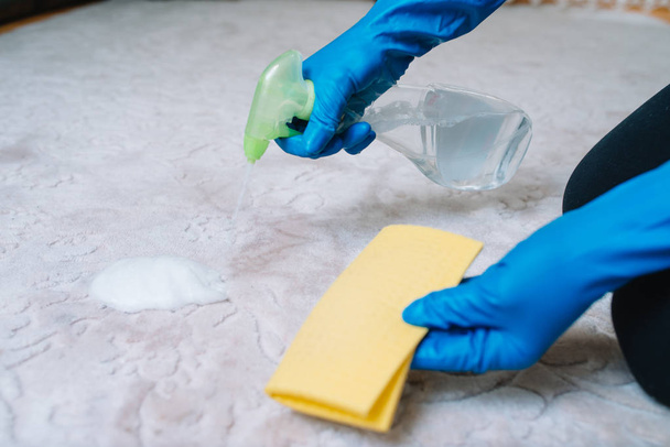 people, housework and housekeeping concept - close up of woman in rubber gloves with cloth and derergent spray cleaning carpet at home. close up of woman with cloth cleaning carpet - Fotó, kép