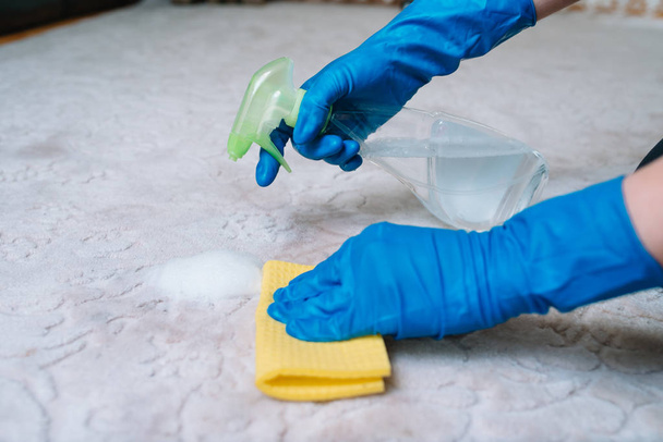people, housework and housekeeping concept - close up of woman in rubber gloves with cloth and derergent spray cleaning carpet at home. close up of woman with cloth cleaning carpet - Foto, afbeelding