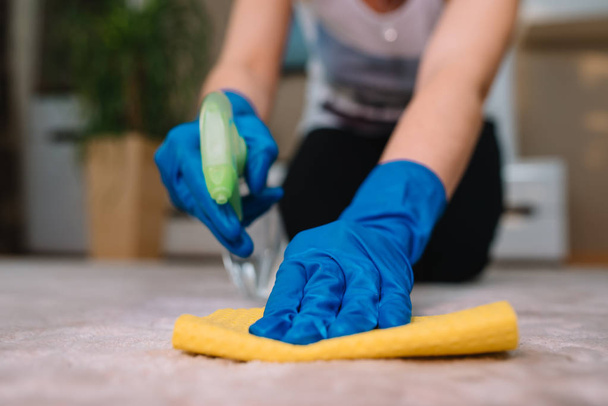 people, housework and housekeeping concept - close up of woman in rubber gloves with cloth and derergent spray cleaning carpet at home. close up of woman with cloth cleaning carpet - Photo, Image