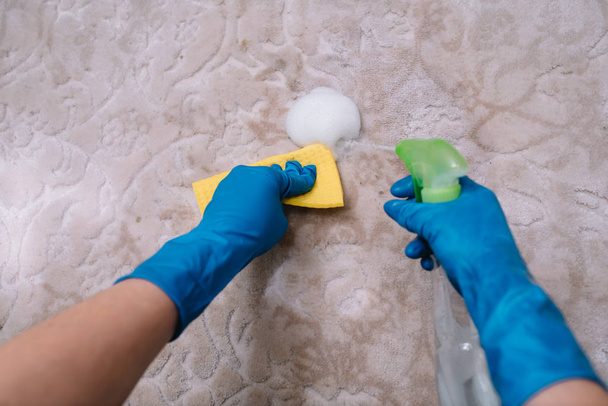 people, housework and housekeeping concept - close up of woman in rubber gloves with cloth and derergent spray cleaning carpet at home. close up of woman with cloth cleaning carpet - Valokuva, kuva