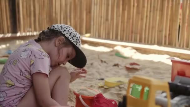 Pieni tyttö leikkii hiekkalaatikossa hiekalla ja leluilla
 - Materiaali, video
