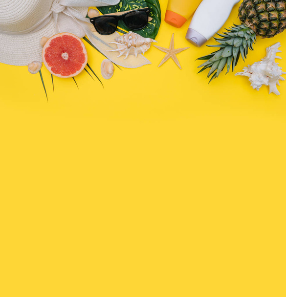 Flat lay beach accessories: swimsuit, sunglasses, hat, sandals with palm branches, exotic fruits and shells. Top view on yellow background - Photo, Image