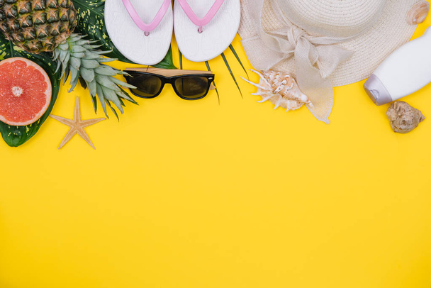 Flat lay beach accessories: swimsuit, sunglasses, hat, sandals with palm branches, exotic fruits and shells. Top view on yellow background - Foto, immagini