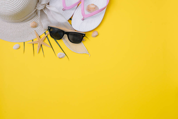 Flat lay beach accessories: swimsuit, sunglasses, hat, sandals with palm branches, exotic fruits and shells. Top view on yellow background - Foto, imagen