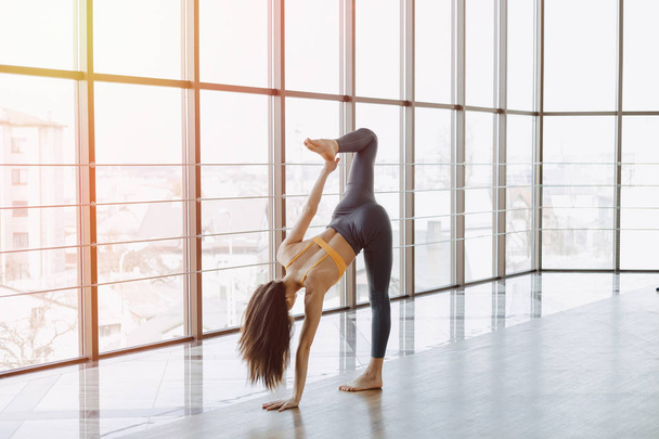 young attractive girl doing fitness exercises with yoga on the floor against the background of panoramic windows - Foto, Imagem