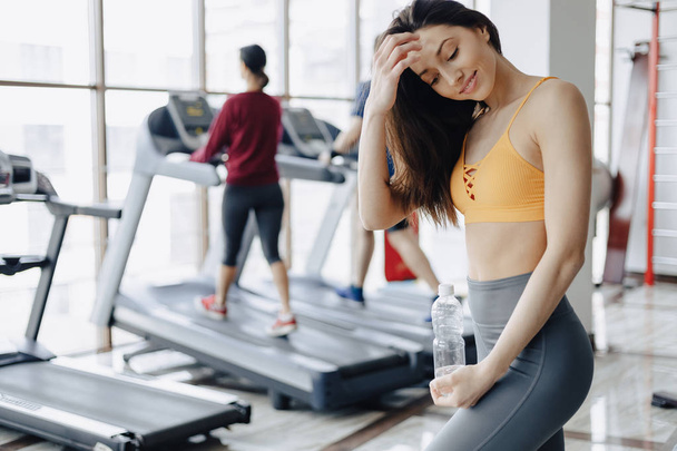 young attractive girl in the gym drinking water on the background of treadmills - Fotó, kép