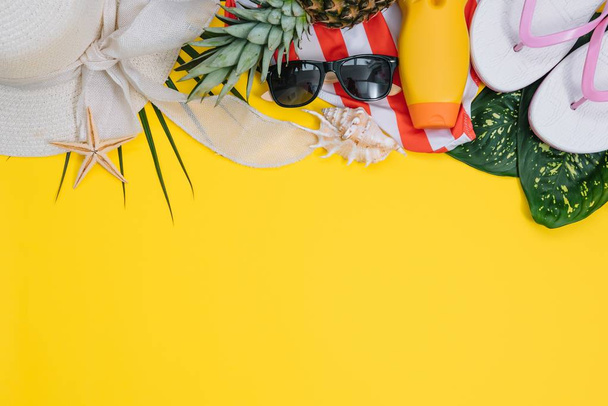 Flat lay beach accessories: swimsuit, sunglasses, hat, sandals with palm branches, exotic fruits and shells. Top view on yellow background - Φωτογραφία, εικόνα