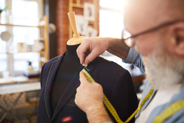 Tailor a darab kréta és mérőszalag jelölés sor gombot lyuk kabát gallérral munka közben stúdióban - Fotó, kép
