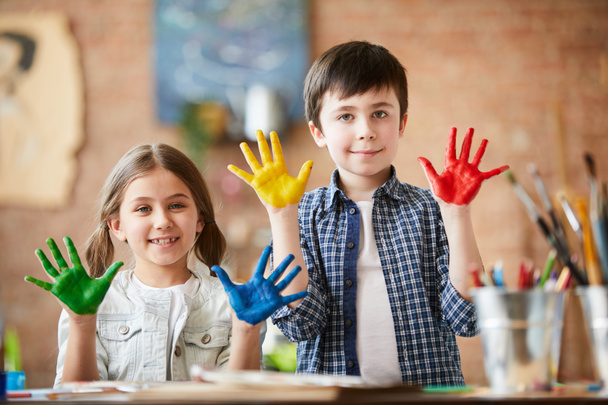 Портрет двух счастливых детей, мальчика и девочки, показывающих руки, окрашенные краской, наслаждаясь классом рисования
 - Фото, изображение