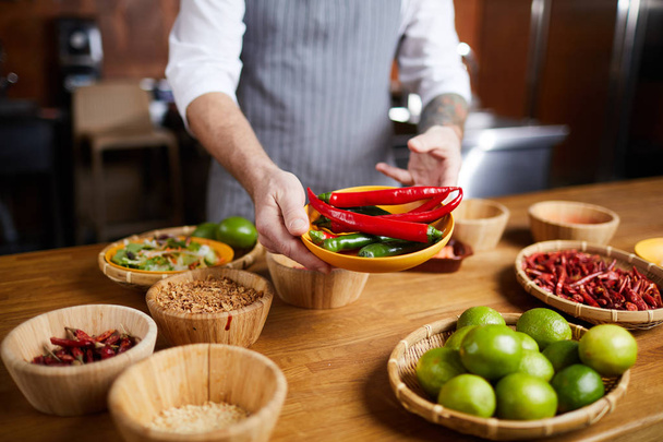 Ritratto di metà sezione di chef professionista che tiene peperoncini e spezie durante la cottura in cucina ristorante, spazio copia
 - Foto, immagini
