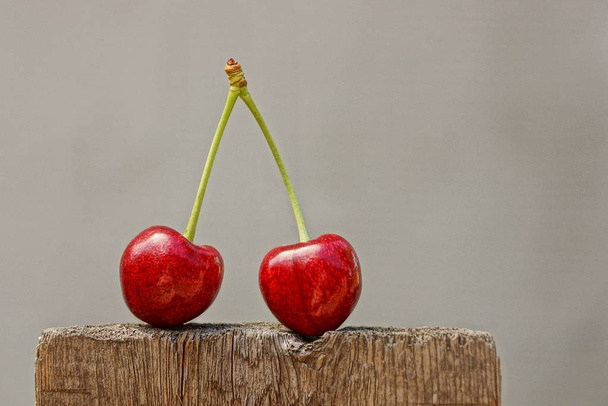 Two ripe red cherries on a gray background - Zdjęcie, obraz