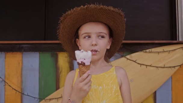 kleines Mädchen mit Strohhut, das draußen auf der Straße Eis isst. Sommerporträt - Filmmaterial, Video