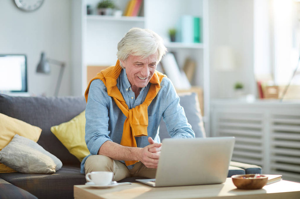 Porträt eines älteren Mannes von heute, der zu Hause glücklich auf den Laptop-Bildschirm lächelt, Kopierraum - Foto, Bild