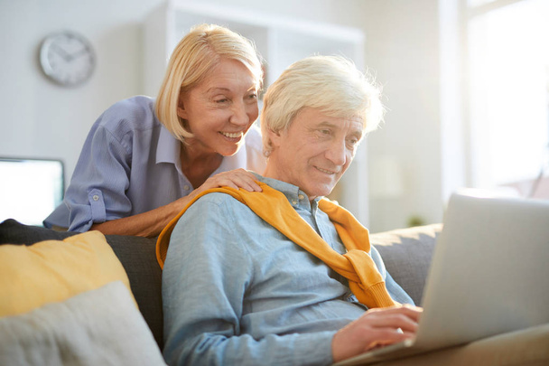 Portrait de couple de personnes âgées contemporaines utilisant un ordinateur portable à la maison éclairé par la lumière du soleil, espace de copie
 - Photo, image