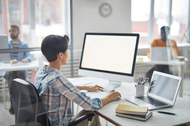 Młody, zajęty menedżer w ubraniach casualwear siedzi przy biurku przed ekranem komputera podczas pracy z danymi online - Zdjęcie, obraz