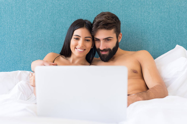 ベッドでリラックスしながら、ノートパソコンの画面上で見て幸せなカップル  - 写真・画像