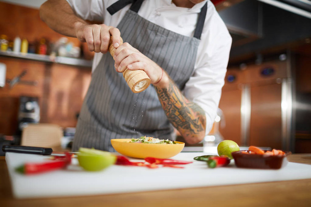 Retrato de sección media del plato profesional de salazón del chef mientras cocina en la cocina del restaurante, espacio para copiar
 - Foto, imagen