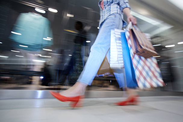 Размытое движение леди-шопоголика с бумажными пакетами в коридоре торгового центра, неизвестная женщина, проходящая мимо витрины магазина
 - Фото, изображение